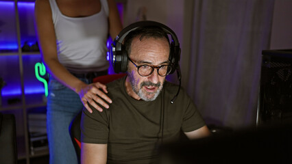 Two gamers, man and woman, intimately bonding over a video game, plugged into the virtual world from their apartment's gaming room.