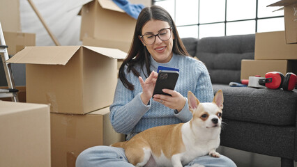 Young hispanic woman with chihuahua dog using smartphone and credit card at new home