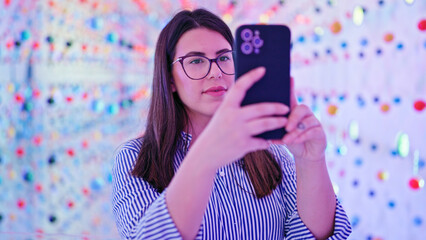 Young beautiful hispanic woman visiting futuristic exhibition space using smartphone