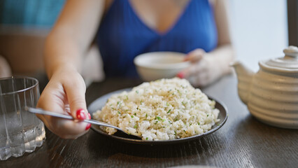 Young woman joyfully eating healthy asian cuisine at a modern restaurant, gourmet rice meal on her plate, deftly handled with a spoon