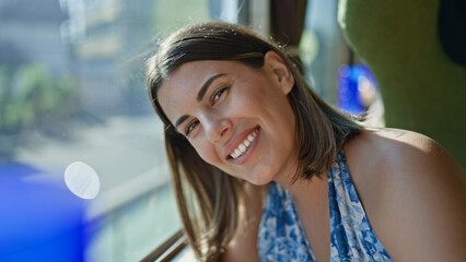 Cheerful, beautiful hispanic woman enjoying her railway journey, smiling while looking through the...