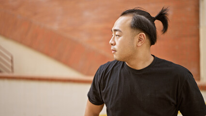 Handsome, cool, young chinese man, with trendy pigtail hairstyle, standing outside on sunny, urban...