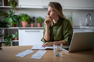 Freelance accountant sits at table, looking at window while thinking over financial statement. Pensive female doing invoices analysis, paperwork, counting company bills and receipts, planning savings