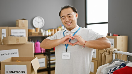 Young, confident chinese volunteer man lovingly smiling, making heartfelt gesture at bustling...