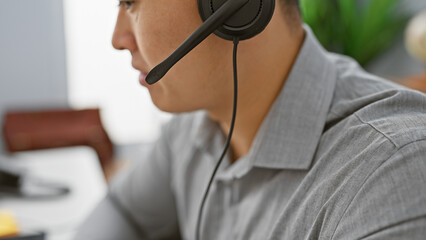 A professional asian man with a headset in a modern office, focused on customer support duties.