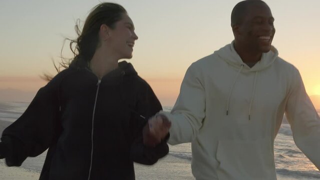 Casually dressed loving young couple walking and running hand in hand along through waves on shoreline watching beautiful sunrise morning over beach and sea in South Africa - shot in slow motion