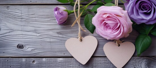 Two heart-shaped wooden ornaments are suspended by a string against a grey wooden backdrop. They are adorned with delicate pink and purple roses, creating a charming and decorative display.