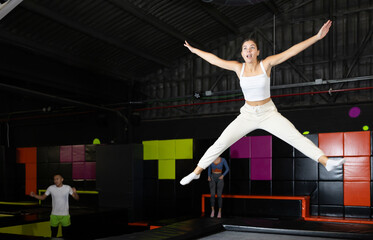 Excited young girl in activewear captured mid-air during fun jump at colorful indoor trampoline center..