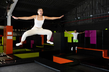 Fototapeta na wymiar Young girl acrobatic athlete jumping and exercising on trampoline indoors, modern hobby and fitness concept