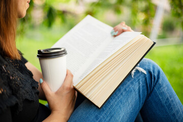 Woman reading book and holding coffee cup in park.