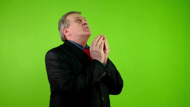 Senior businessman prays with arms raised up and folded palms.