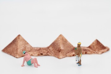 miniature people of men standing on a beach with egyptian pyramids on background