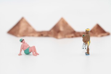 miniature people of men standing on a beach with egyptian pyramids on background