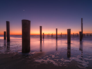 A seascape during sunset. Pillars on the seashore. Bright sky during sunset. Reflections on the seashore. A sandy beach at low tide. Travel image. - 745426750