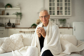 A man with glasses drinks tea and warms himself on the sofa in the kitchen.