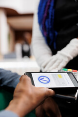 Male hotel guest making cashless payment using smartphone, phone and card reader machine, close up....