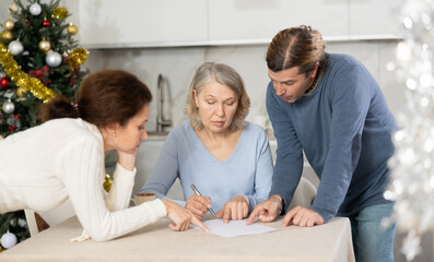 Man and woman help and advise elderly mother on how to make covenant while at home in kitchen...