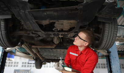 Auto mechanic working in garage. Repair service. Worker mechanics in uniform are working in auto service with lifted vehicle. Car repair maintenance.