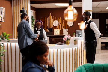 Friendly welcoming female receptionist helping tourist with check-in procedure at front desk. African American hotel staff assisting guest at reception, customer service in hospitality industry