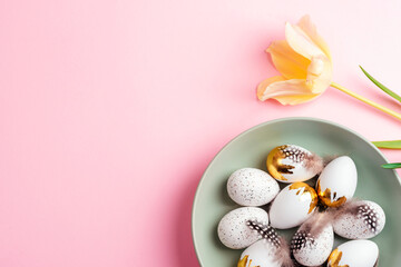 Easter eggs on green plate and yellow tulip on pink background. Top view, flat lay, copy space