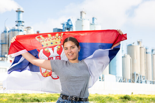Cheerful girl with serbian flag standing in front of factory