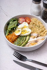 A bowl of couscous, meat, eggs and vegetables angle view on grey background.