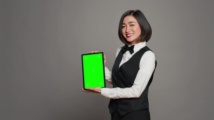 Woman concierge presenting greenscreen display on tablet, showing chromakey template on screen. Receptionist with bow and uniform holding device with blank copyspace layout. Camera A.
