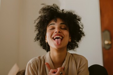 A woman sticks out her tongue with a funny expression, hands clasped.