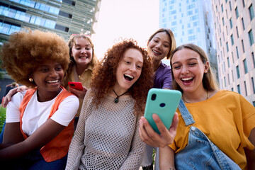 Young group of gen z people having fun surprised using cell phone together outside watching something funny at mobile. Cheerful community of student enjoying social media content. Multiethnic friends