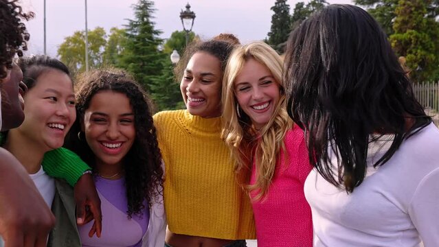 Young diverse group of happy girls laughing together at city street. Female friendship concept with millennial women having fun hugging each other outdoors.