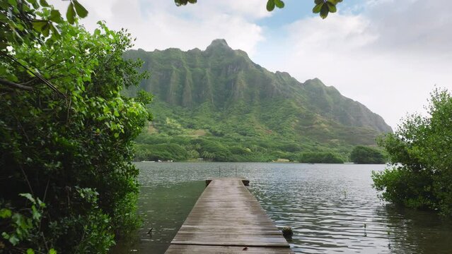 Epic landscapes on Oahu island. Secret beach filming location with pond. Dramatic cloudy morning on Hawaii island. Drone flying low above wooden boat pier with cinematic Jurassic nature mountain ridge