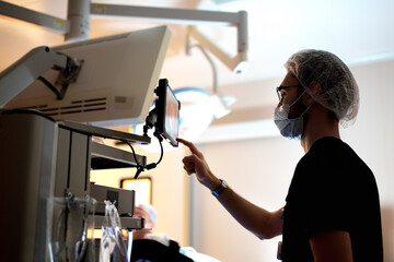 An assistant intern monitors the progress of a surgical operation on a portable screen in operating room in modern medical hospital. - obrazy, fototapety, plakaty