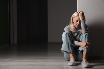Depressed mature woman sitting in dark hall - obrazy, fototapety, plakaty