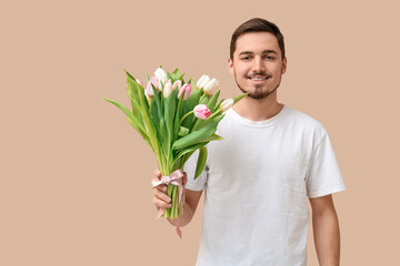 Happy young man with bouquet of beautiful tulips on beige background. International Women's Day