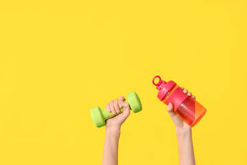 Female hands with dumbbell and bottle of water on yellow background