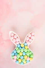 Pastel candy coated chocolate eggs in an Easter Bunny shaped white ceramic dish against a vibrant multi-shade pink background
