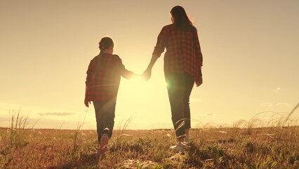 Happy family, Mother, child daughter, walk hand in hand at sunset in field. Family walk outdoors....