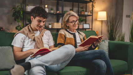 Mother and teenage son man and woman sit at home on sofa bed read book