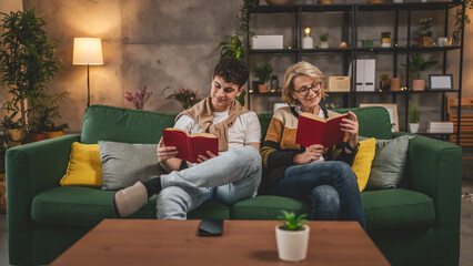 Mother and teenage son man and woman sit at home on sofa bed read book