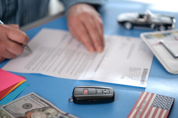 Close-up of a car key fob and the hands of a businessman filling out a car purchase agreement with...