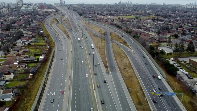 Aerial view of a drone flying over Highway 401 in Toronto on a cloudy day. The drone is moving towards a couple of road junctions that have slightly busy traffic.