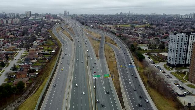 Aerial shot of a drone moving across Highway 401 in Toronto on a cloudy day. The drone is approaching a couple of road junctions that with slightly busy traffic.
