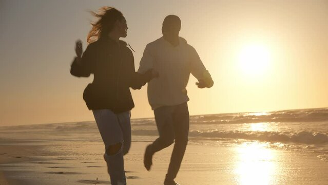 Casually dressed loving young couple running hand in hand along shoreline watching beautiful sunrise morning over beach and sea in South Africa - shot in slow motion