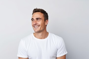 Portrait of handsome young man in white t-shirt looking away and smiling while standing against grey background