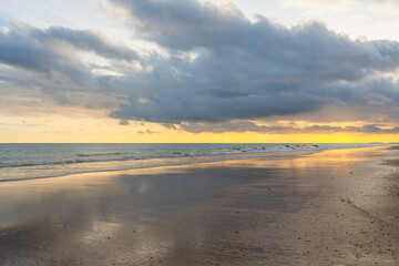 Sunset paints the cloudy sky in warm hues over a tranquil beach