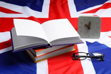 Learning foreign language. Different books, alarm clock and glasses on flag of United Kingdom