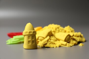 Castle figures made of yellow kinetic sand on grey background, closeup. Space for text