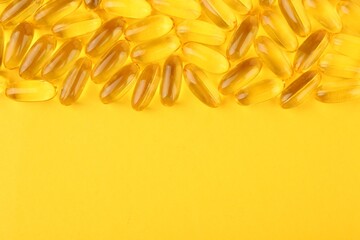 Many vitamin capsules on yellow background, top view. Space for text