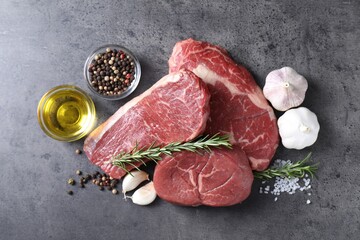 Raw beef steaks, oil and spices on grey table, flat lay