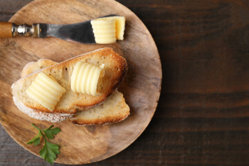 Tasty butter curls, knife and slices of bread on wooden table, top view. Space for text